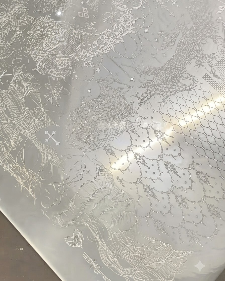 Przezroczysty stempel naciskający na metalową blaszkę wypełnioną misternymi białymi wzorami koronek.