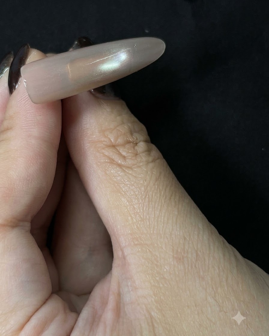 Gotowe, długie przedłużenie paznokcia cat-eye w odcieniu nude trzymane na ciemnym tle, ukazujące miękką, odblaskową linię pośrodku.