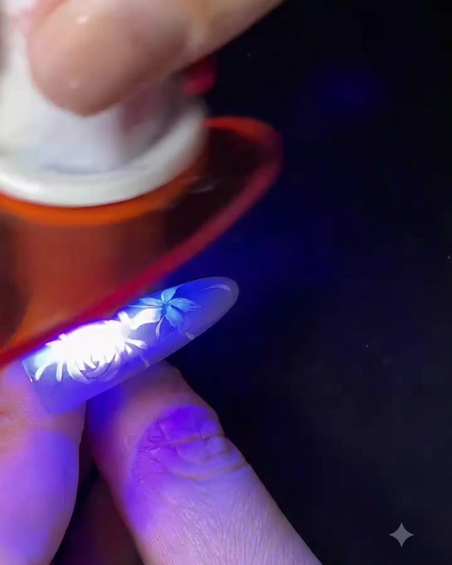 Palec z ukończonym białym kwiatowym zdobieniem paznokci utwardzany pod małą niebieską lampą UV/LED.