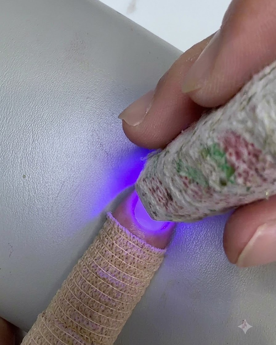 Wzorzysta mini lampa UV/LED trzymana nad końcówką paznokcia podczas utwardzania warstwy przezroczystego żelu.