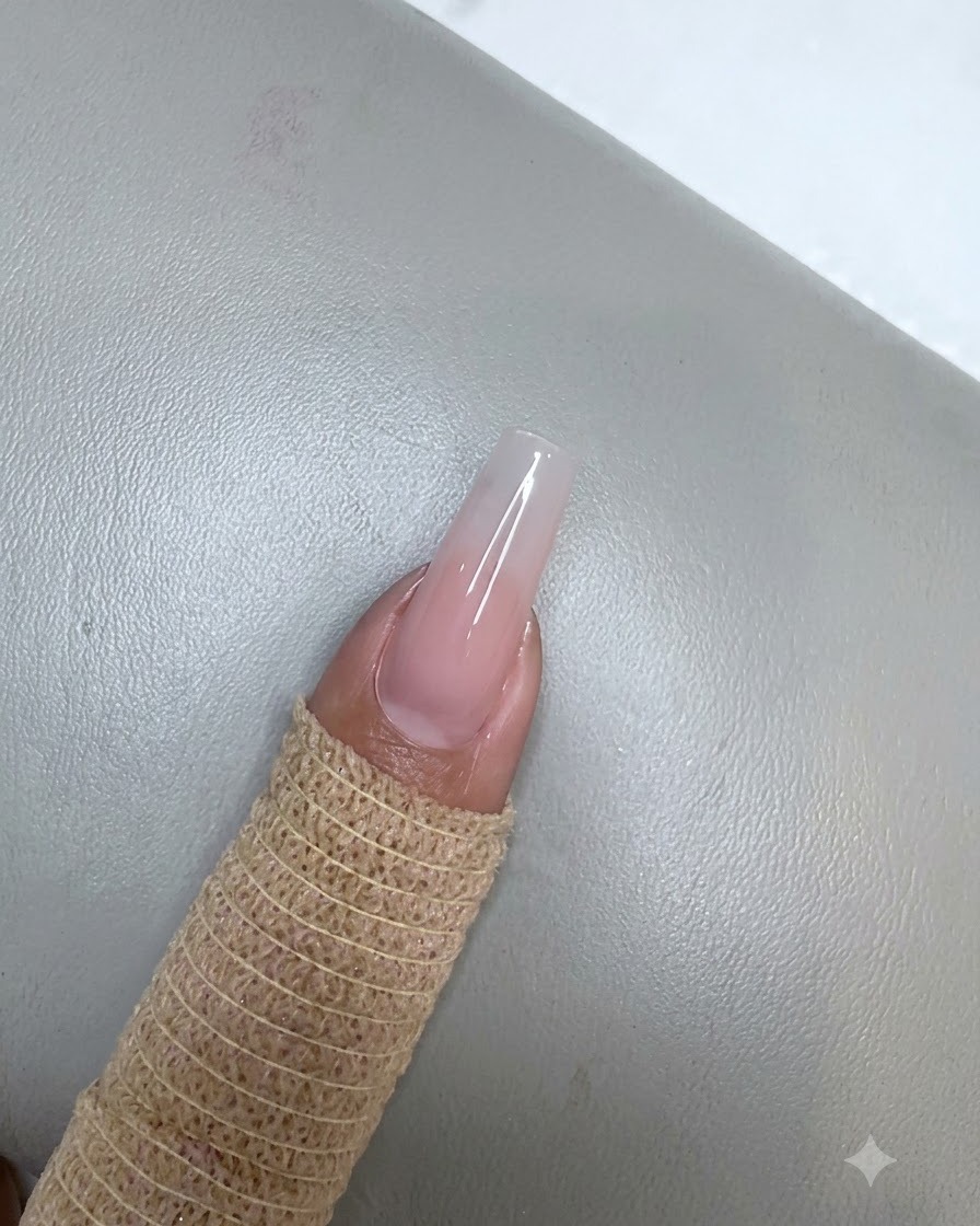 Paznokieć z utwardzoną warstwą różowego żelu nude spoczywający pod małą fioletową lampą UV LED.