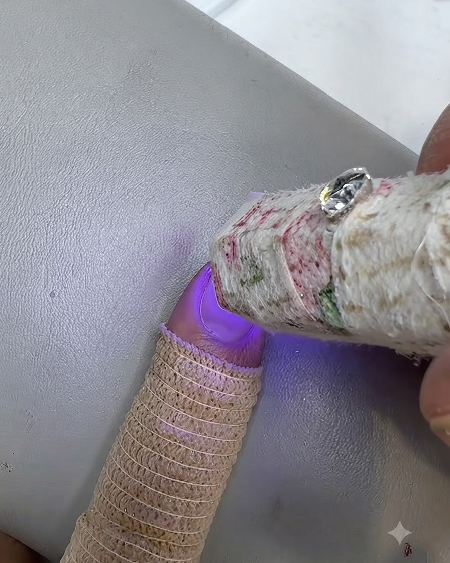 Mała lampa UV utwardzająca pomalowany paznokieć, przy palcu widoczna jest dzianinowa osłonka.