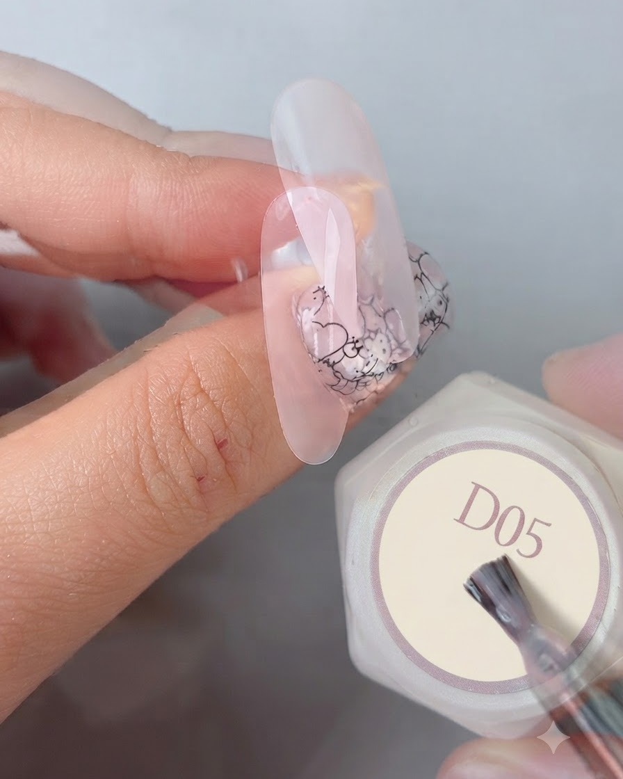 Pędzelek do manicure nakładający ostateczny, błyszczący, gładki top na gotowy wzór paznokcia obok buteleczki żelu oznaczonej D05.