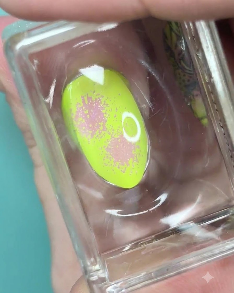 Czysty silikonowy stempel trzymający neonowo-zielony paznokieć z miękkim różowym gradientem i nakrapianą teksturą.