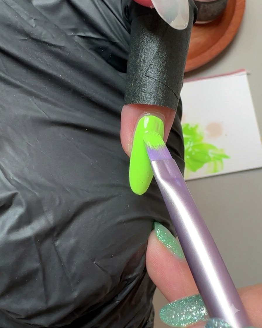 Pędzelek nakładający fluorescencyjny zielony żel na paznokieć małego palca.