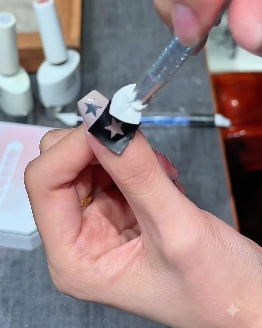 Stempel z gąbki nakładający mlecznobiały żel na naklejkę pustej gwiazdy na paznokciu.