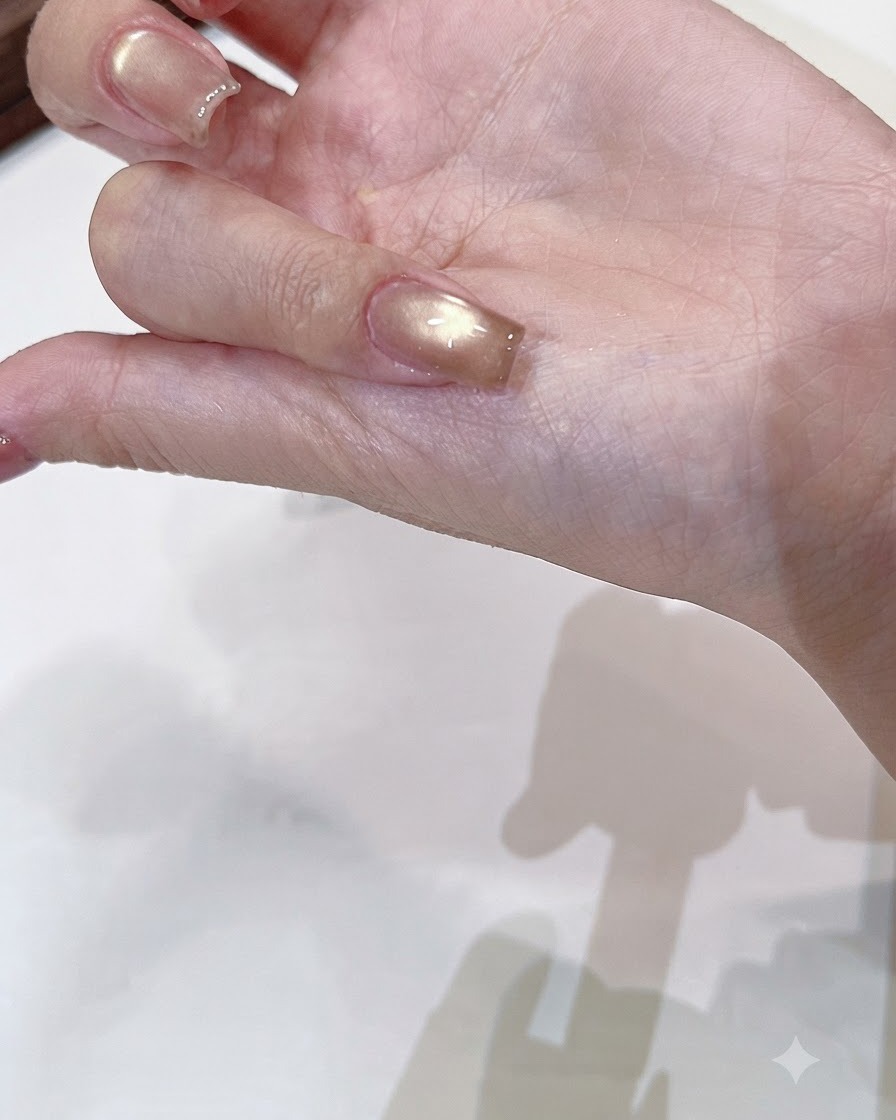 Pędzelek nakładający bezbarwny, lśniący top coat na utwardzony szampańsko-złoty paznokieć cat-eye.