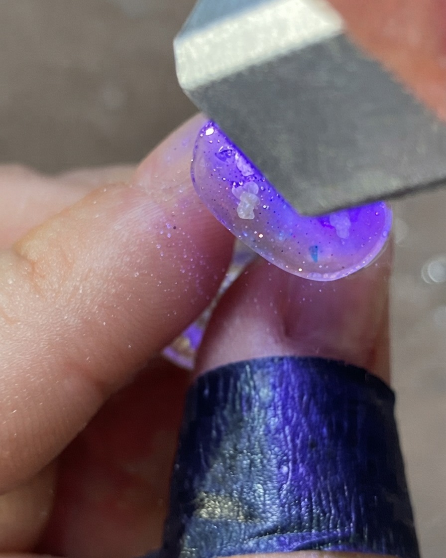 Dłoń pod fioletową lampą UV/LED utwardzająca ozdobiony wzór paznokcia.