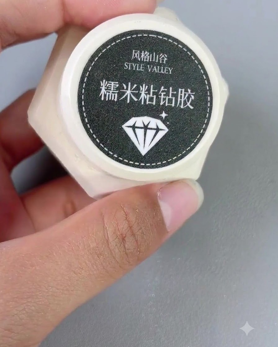 Niewielki pojemniczek z żelem typu sticky diamond trzymany w dłoni obok pędzelka do paznokci.