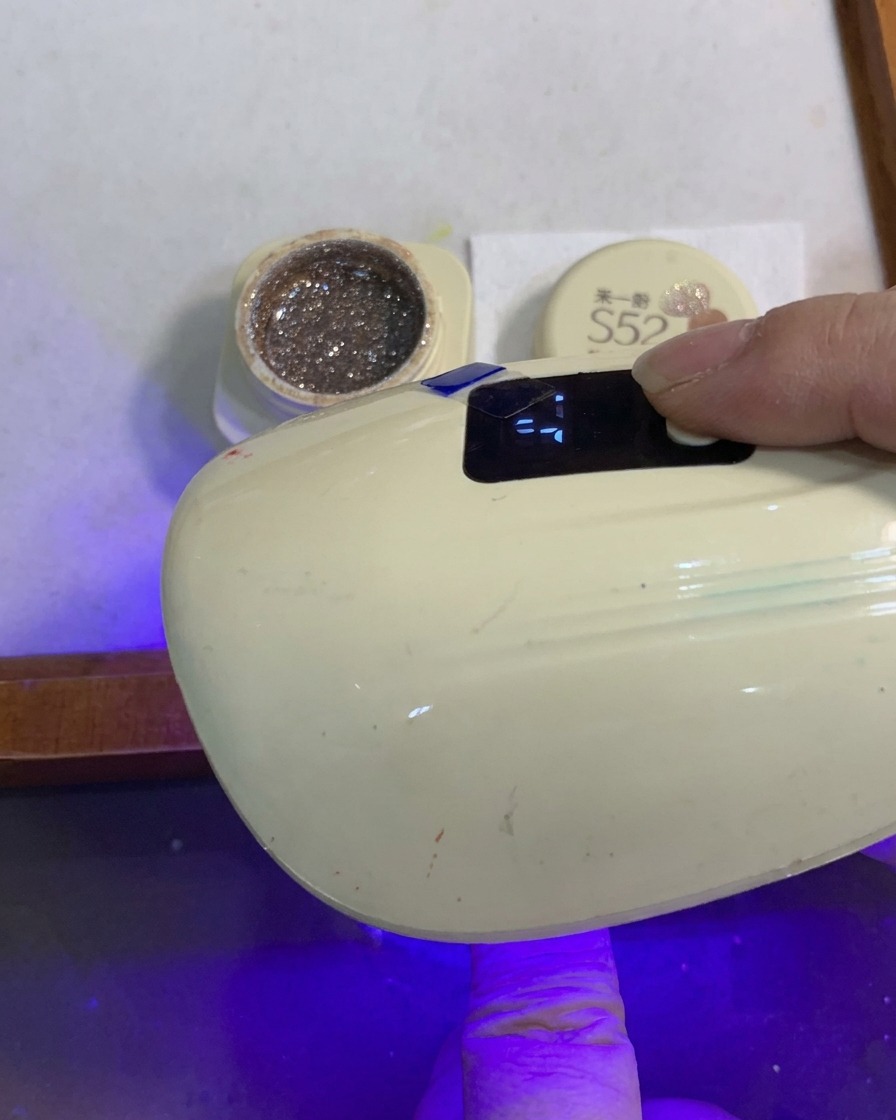 Palec z brokatowym gradientem utwardzany w małej, przenośnej lampie UV/LED.