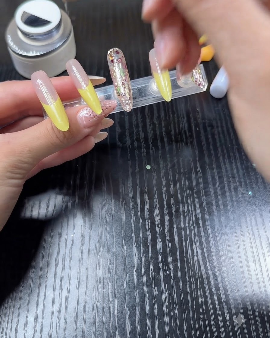 Pędzelek nakładający przezroczysty top coat na paznokieć z jasnym, żółtym frenchem.
