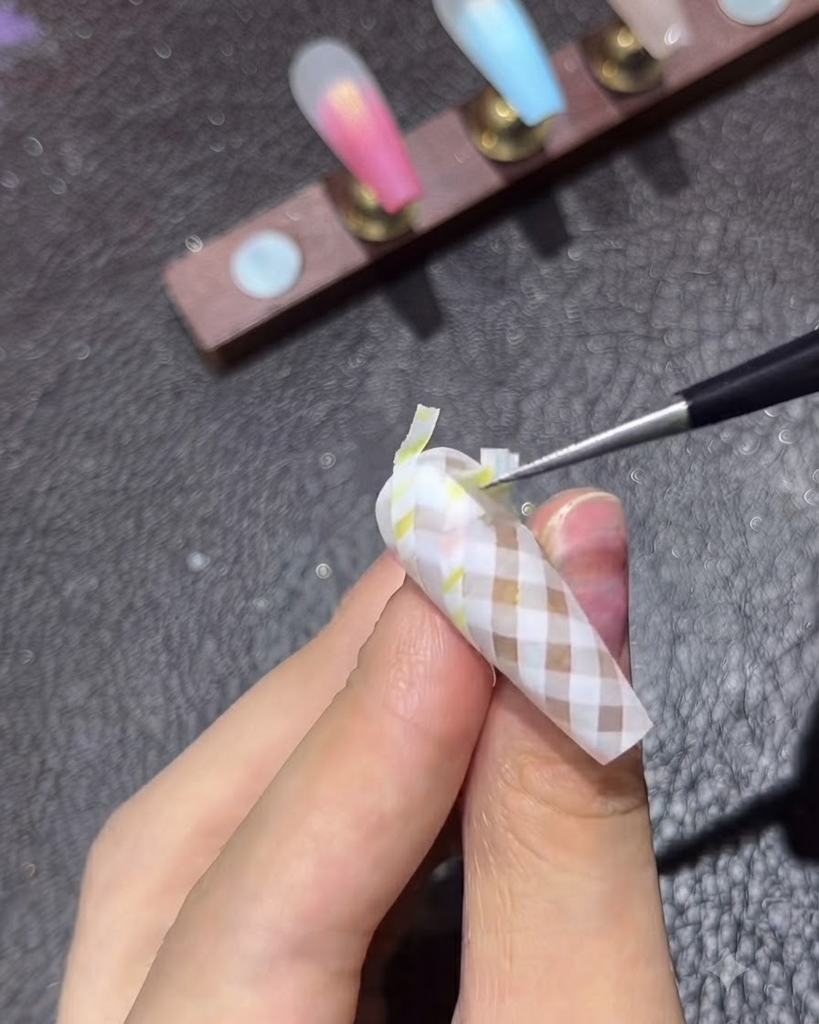 Cienki pędzelek do zdobień nakładający błyszczący top coat na ukończony brązowy wzór w kratę.