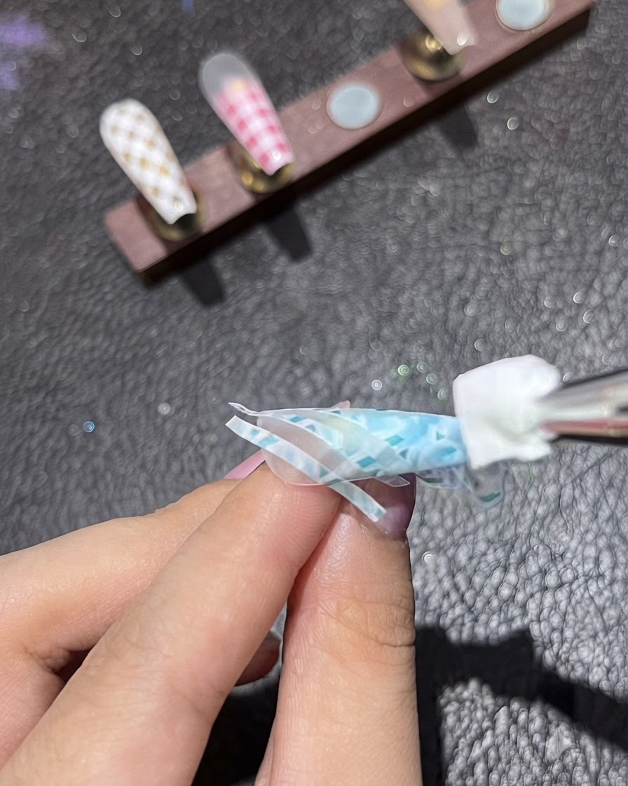 Gąbka wklepująca biały pigment na drugi zestaw taśm dekoracyjnych na niebieskim paznokciu.
