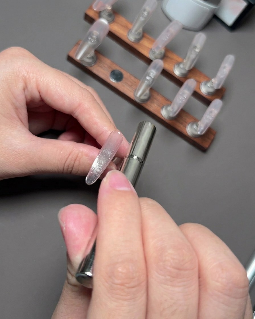 Magnetická palička vznášajúca sa v blízkosti nechtu na zhromaždenie a vytvarovanie reflexných cat-eye častíc.