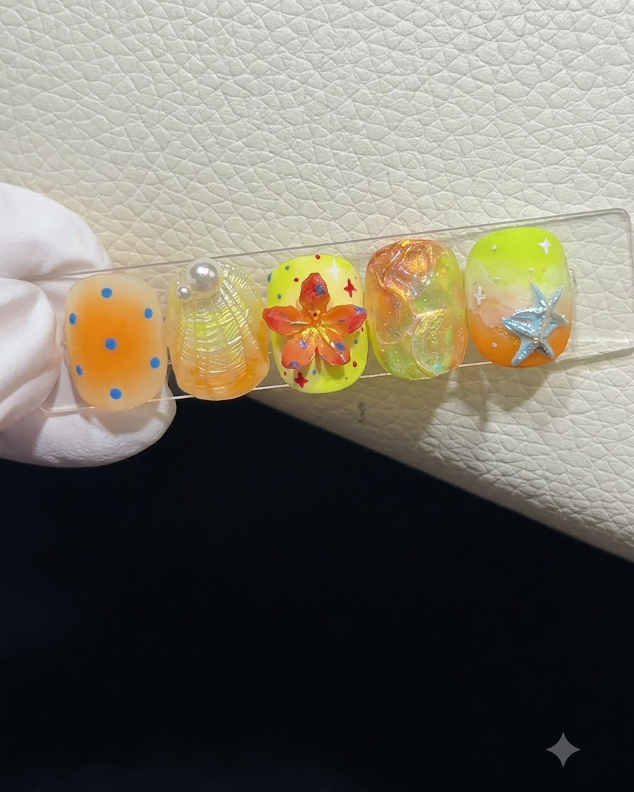 Zbliżenie na stojak ekspozycyjny prezentujący pięć letnich sztucznych paznokci z różnymi teksturami 3D i zdobieniem.