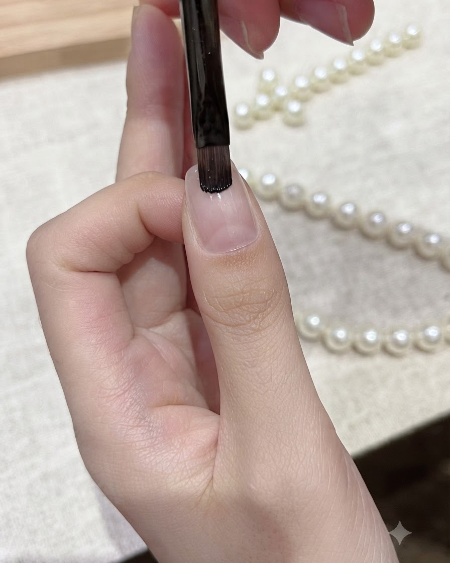 Ein flacher Gelpinsel trägt schwarzen Gellack auf die freie Kante eines Naturnagels auf.