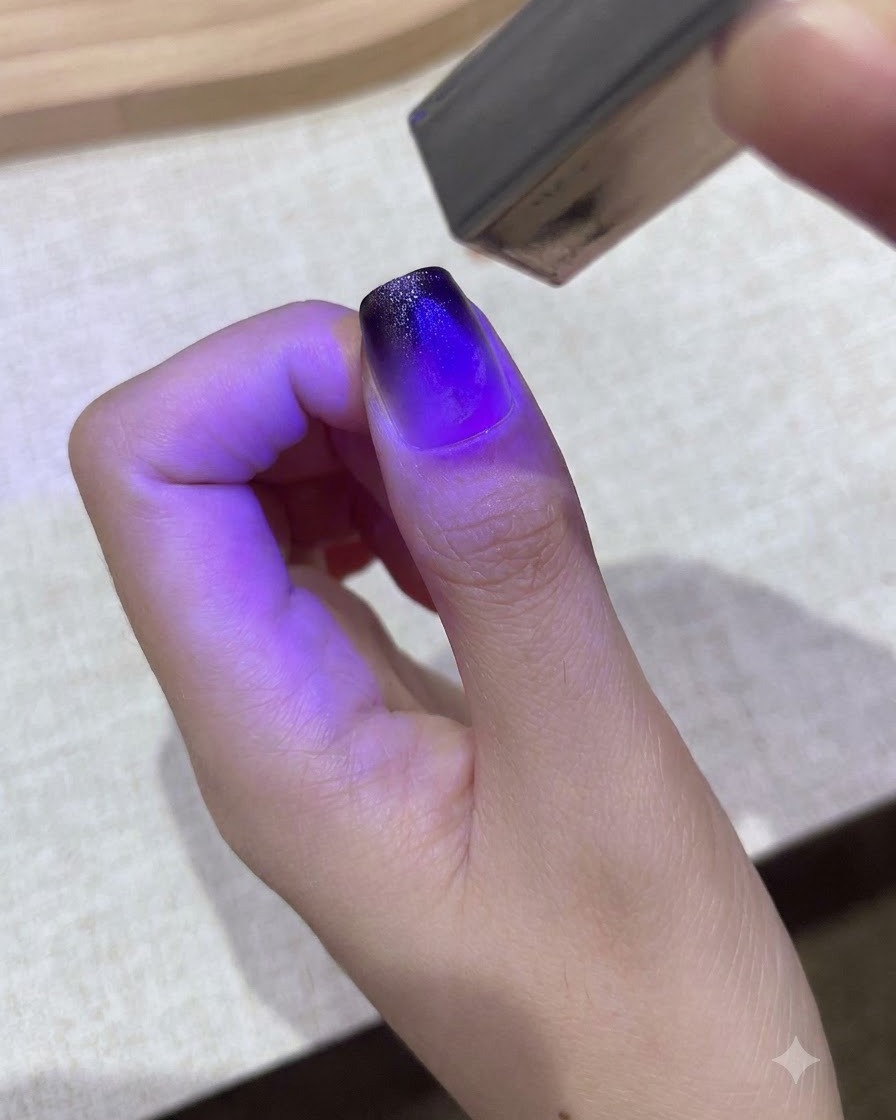 Eine kleine lila Hand-UV/LED-Lampe härtet ein Gradienten-Gel-Design auf einem Daumennagel aus.