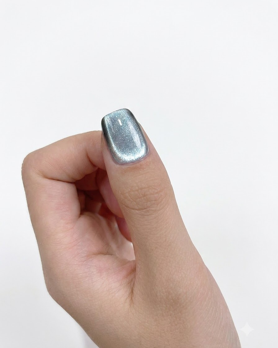 Eine Nahaufnahme eines zylindrischen Magneten, der präzise an der linken Seite eines lackierten Nagels gehalten wird.