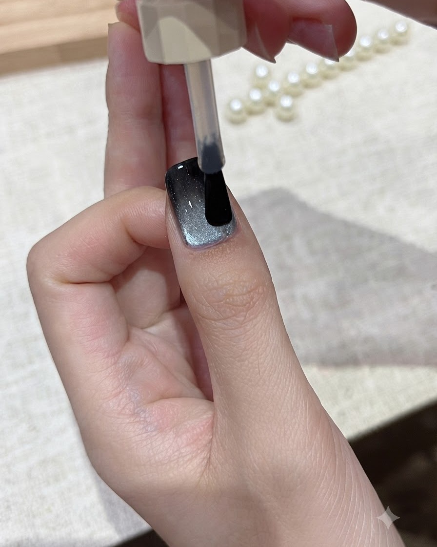 Ein Pinsel lässt eine Schicht klaren Glanz-Überzugs über das fertige Cat-Eye-Nageldesign gleiten.