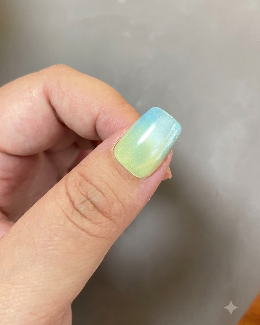 Ukończony żelowy manicure z niebiesko-żółtym gradientem i świecącym wzorem pierścienia w miękkim oświetleniu.