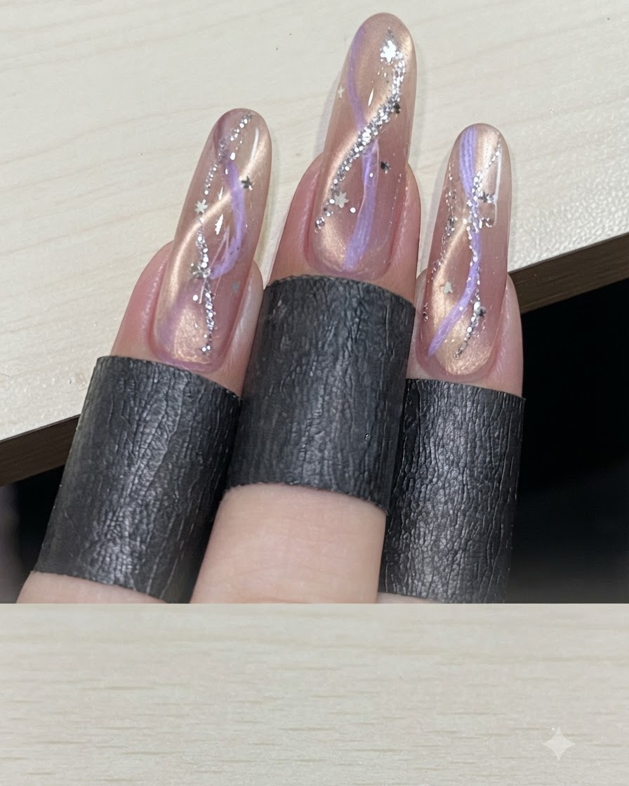 Widok wielu palców prezentujący ukończone manicure cat-eye ze wstążką, ozdobione srebrnymi cekinami w kształcie gwiazdek.