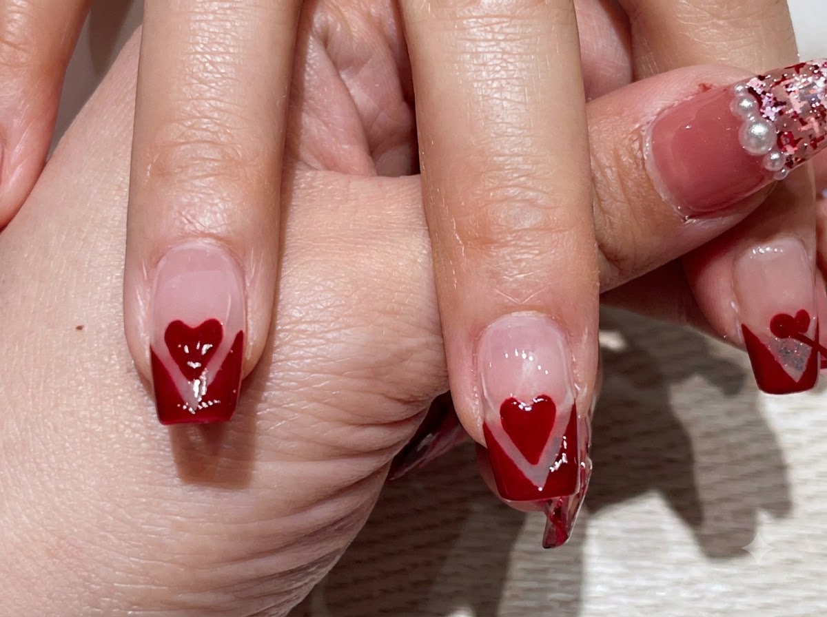 Zbliżenie dłoni prezentującej palce z czerwonym manicure French typu V-tip i wyśrodkowanymi czerwonymi sercami.