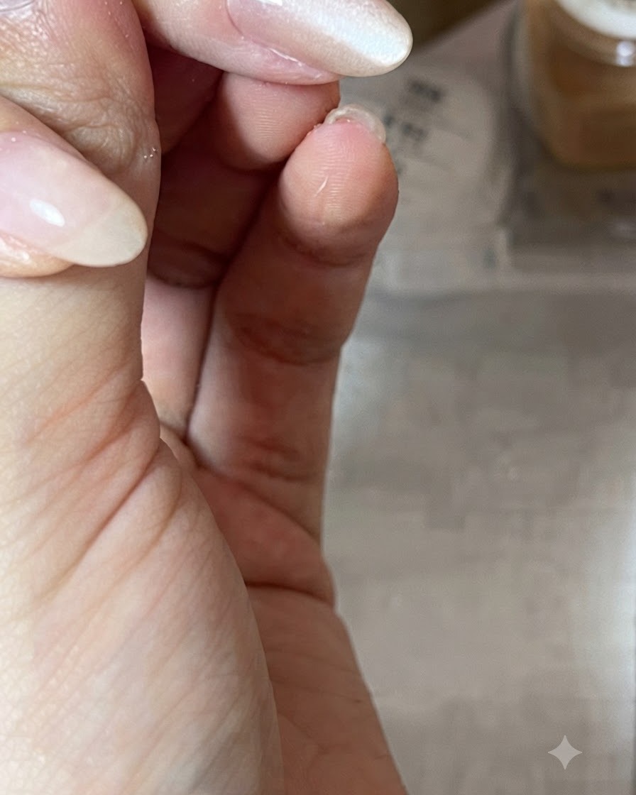 Zbliżenie dłoni trzymającej magnes ukośnie nad błyszczącym paznokciem w odcieniu nude pomalowanym żelem cat-eye, aby uformować refleks świetlny.