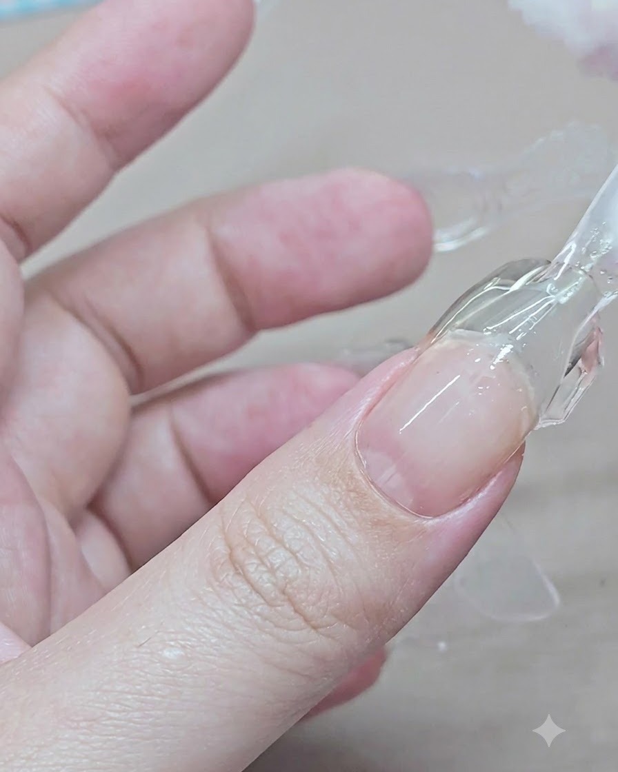 Dłoń ściskająca i podważająca przezroczystą plastikową dual formę z utwardzonego przedłużenia żelowego na palcu wskazującym.