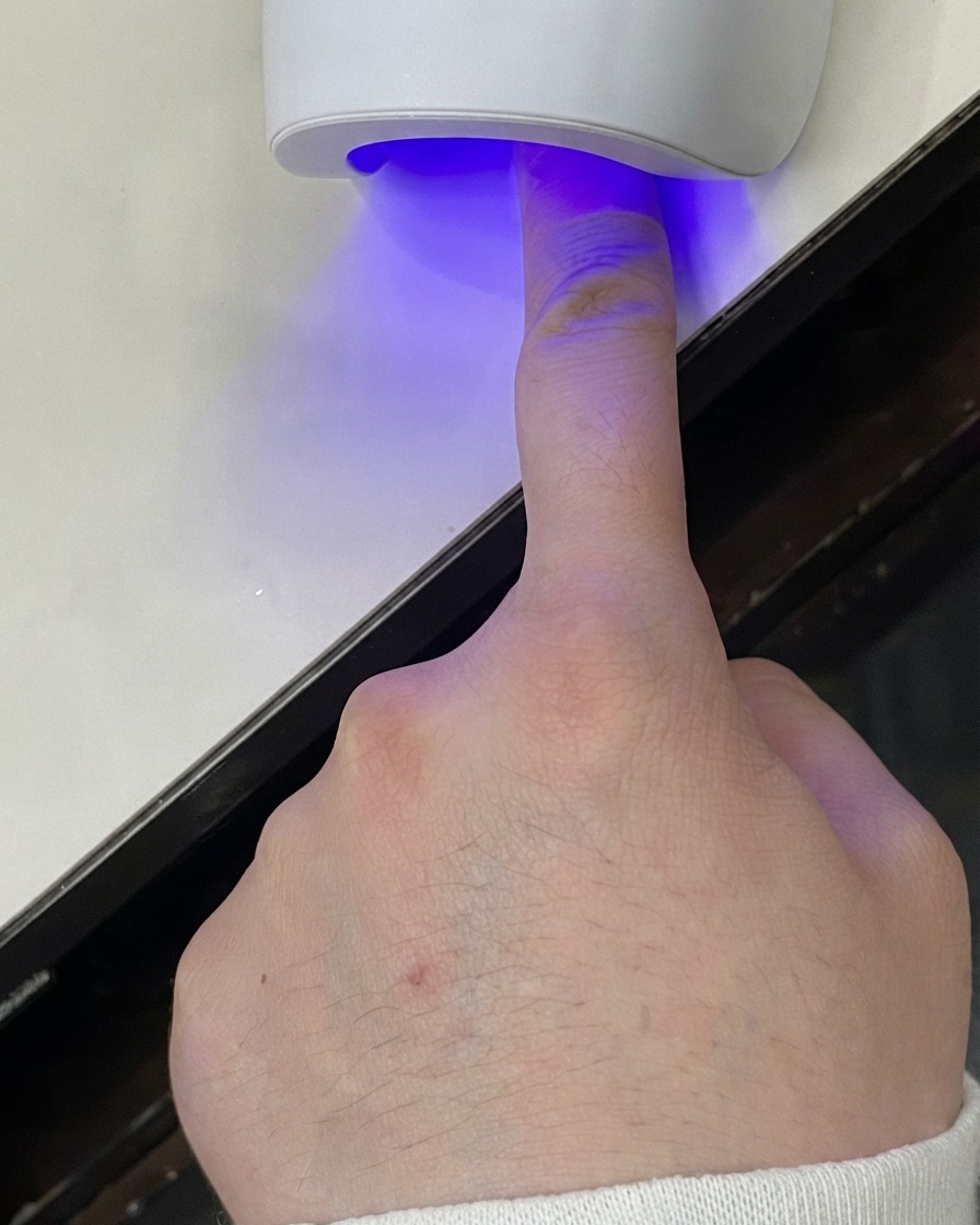 Palec umieszczony pod mini lampą UV LED utwardzającą warstwę żelu.