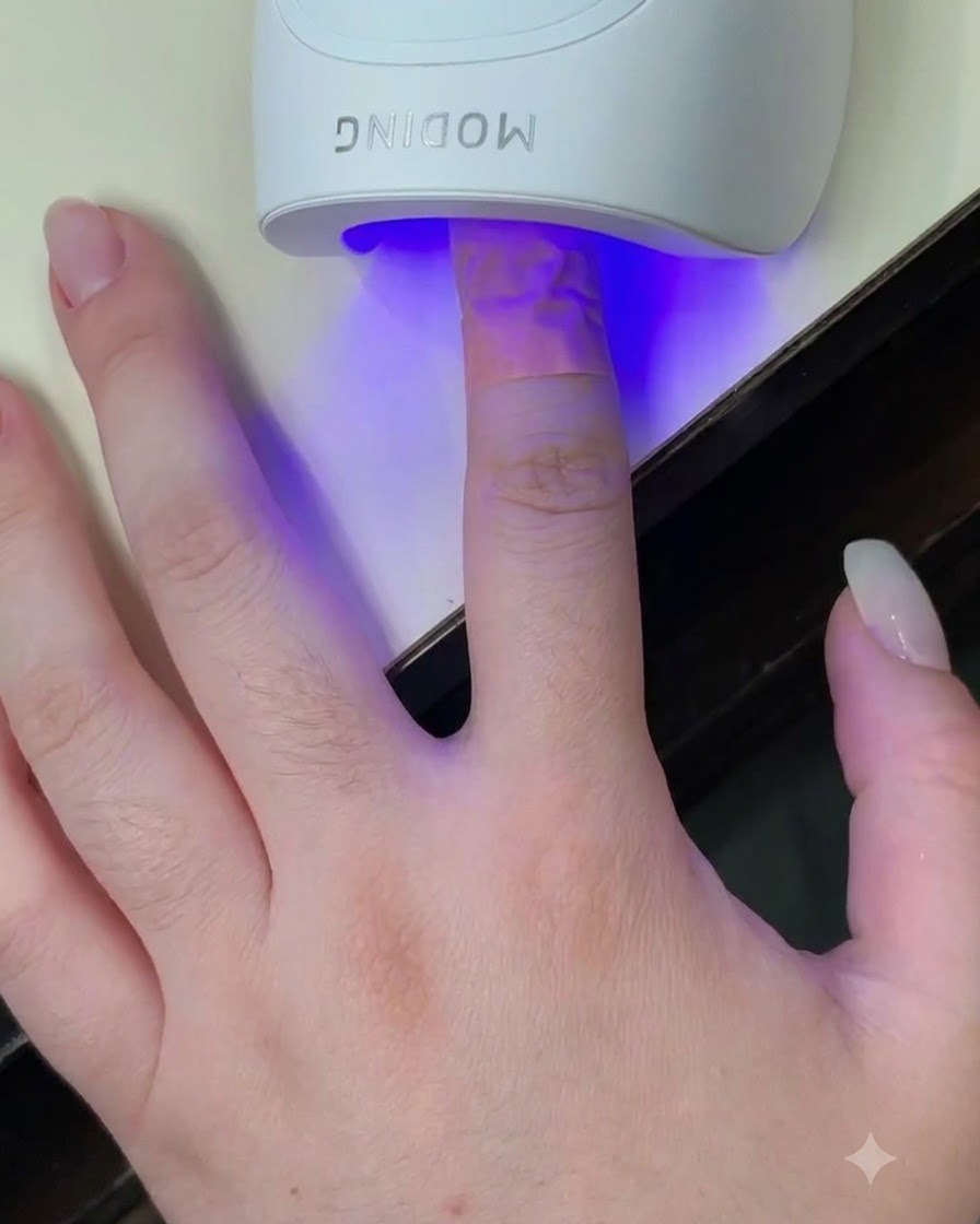 Palec umieszczony w białej mini lampie UV LED z niebieskim światłem padającym na paznokieć.