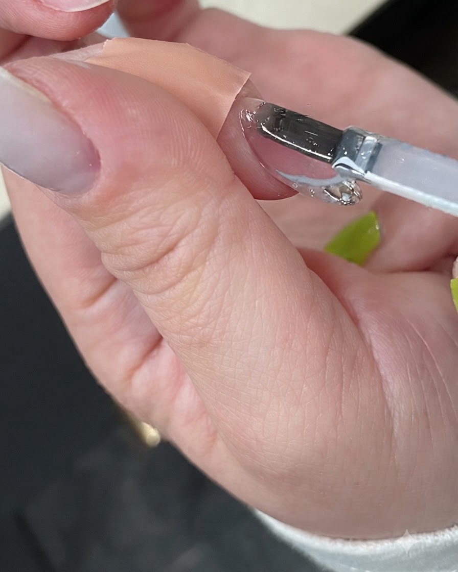 Dłoń utwardzająca gotowy manicure wewnątrz kompaktowej białej lampy UV do paznokci.