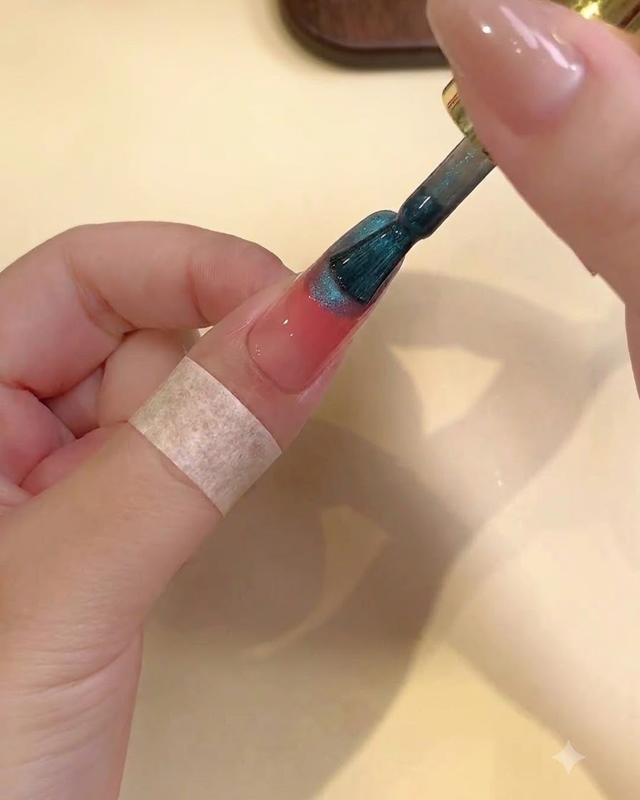 Pędzelek aplikujący mieniący się turkusowy żel cat-eye na górną część różowego paznokcia blush.