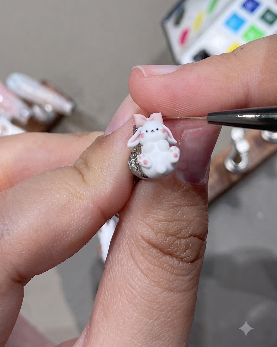 Zbliżenie na szczegółową zawieszkę 3D w kształcie króliczka z różowymi uszkami i małą kokardką, nad którą pracuje się za pomocą precyzyjnego narzędzia.