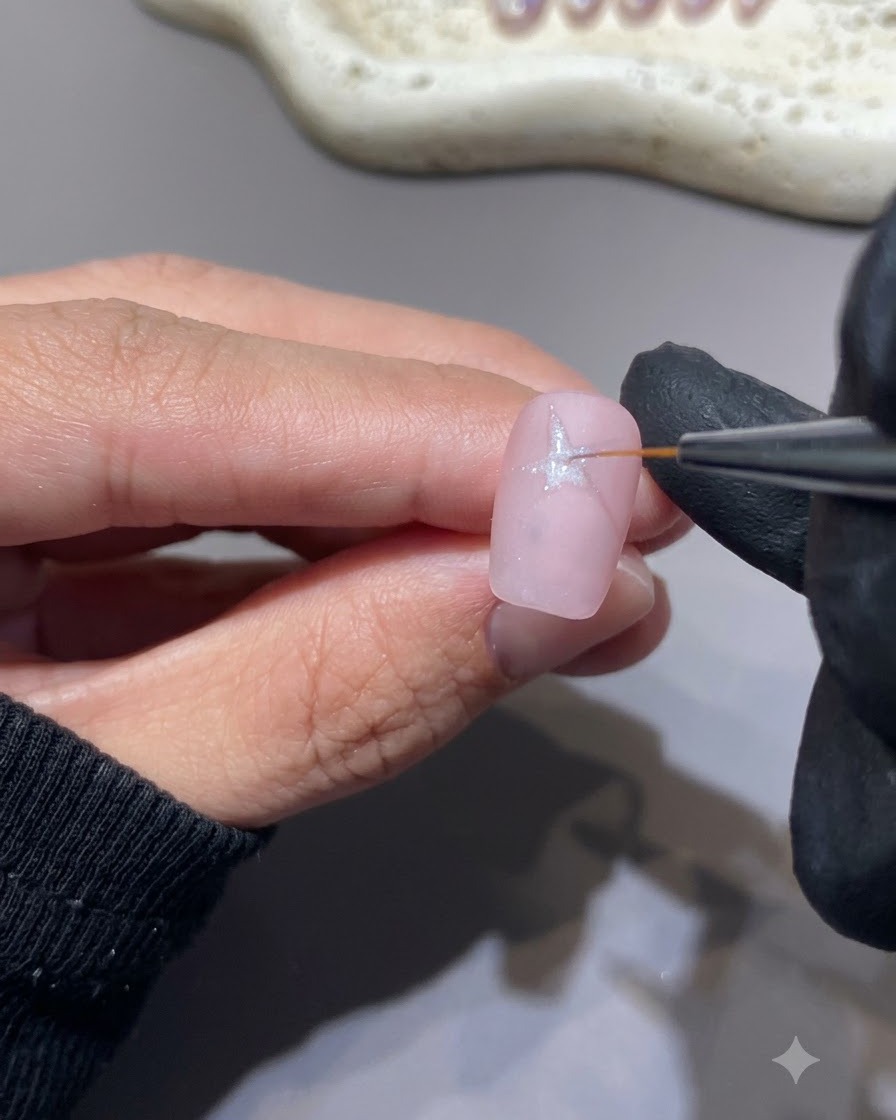 Ein feiner Liner-Pinsel malt eine weiße Sternform auf eine rosa Nageloberfläche.