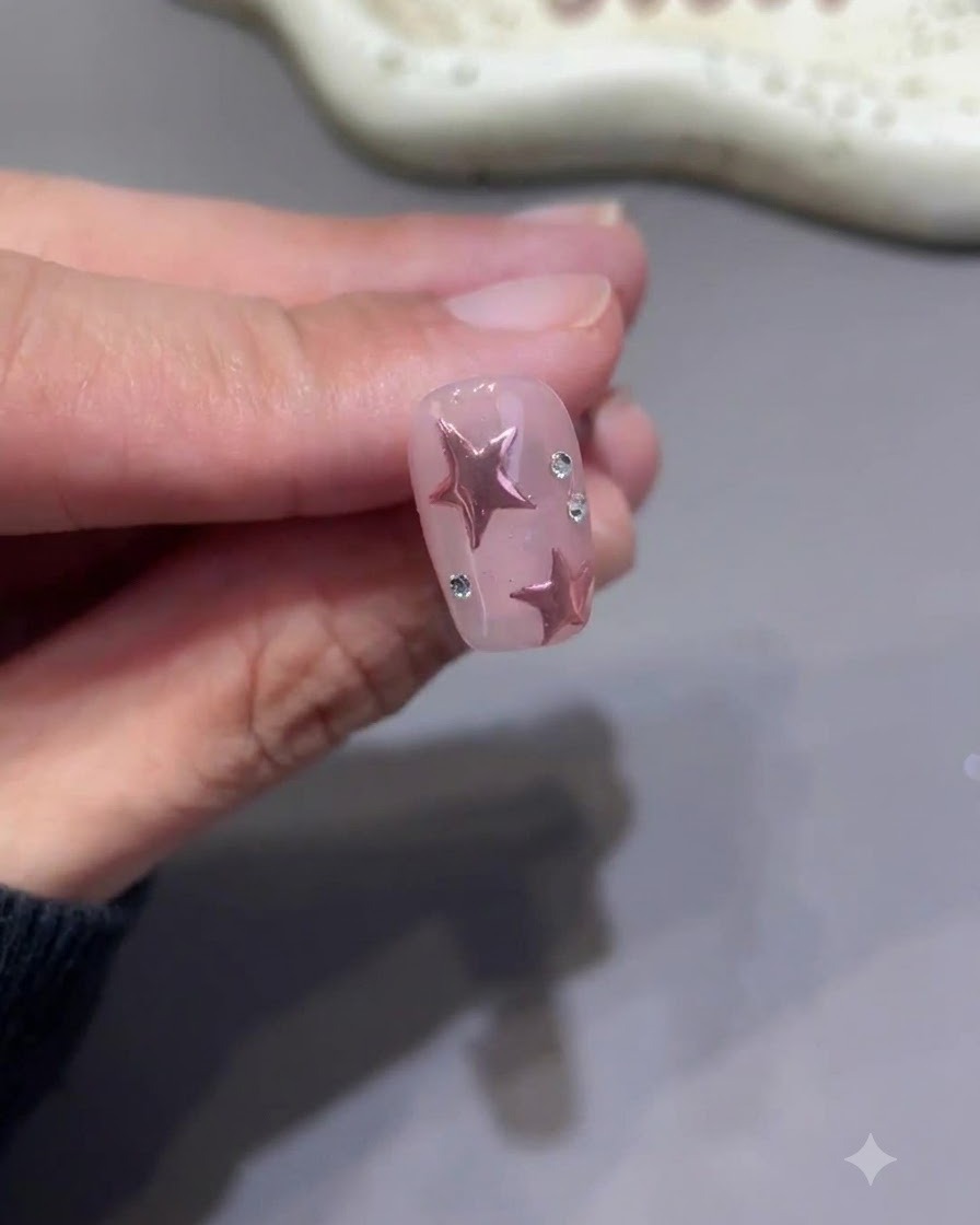 Ein winziger Detailpinsel zieht sorgfältig Top Coat um die Basis kleiner Strasssteine an einem fertigen rosa Sternennagel.