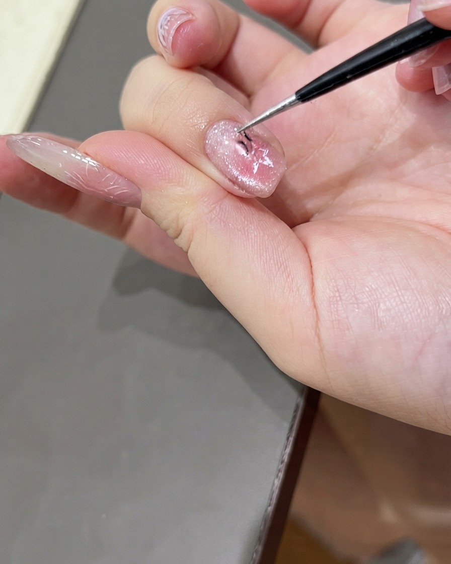 Para precyzyjnych pęset delikatnie zdejmująca naklejkę w kształcie gwiazdy z błyszczącego paznokcia pomalowanego żelem cat eye.
