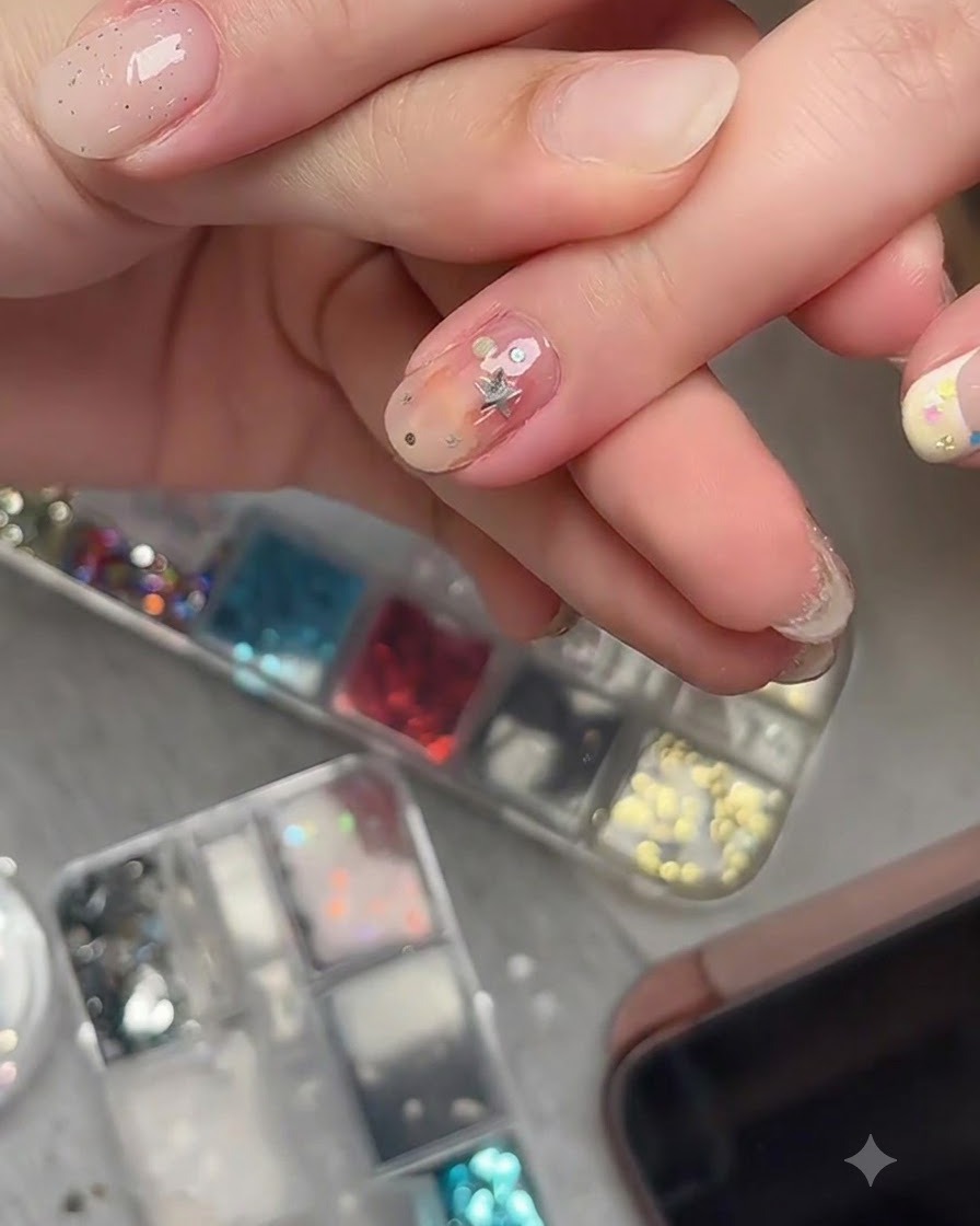 Pędzelek do nail art aplikujący bezbarwny top coat na zatopione ozdoby z gwiazdek na gotowym paznokciu.