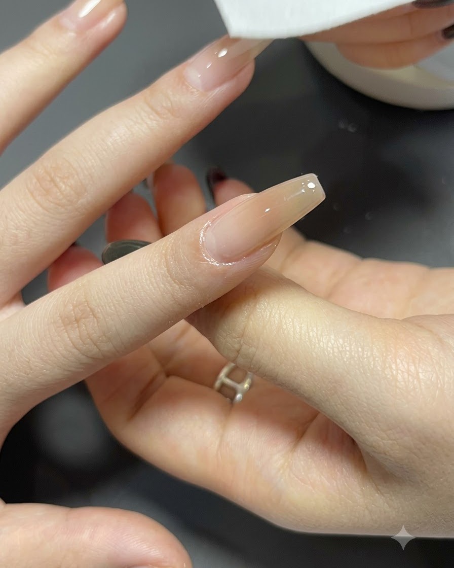 Ein fusselfreier Tupfer reinigt die Oberfläche eines langen, sargförmigen Nagels mit einem fertigen Farbverlauf.