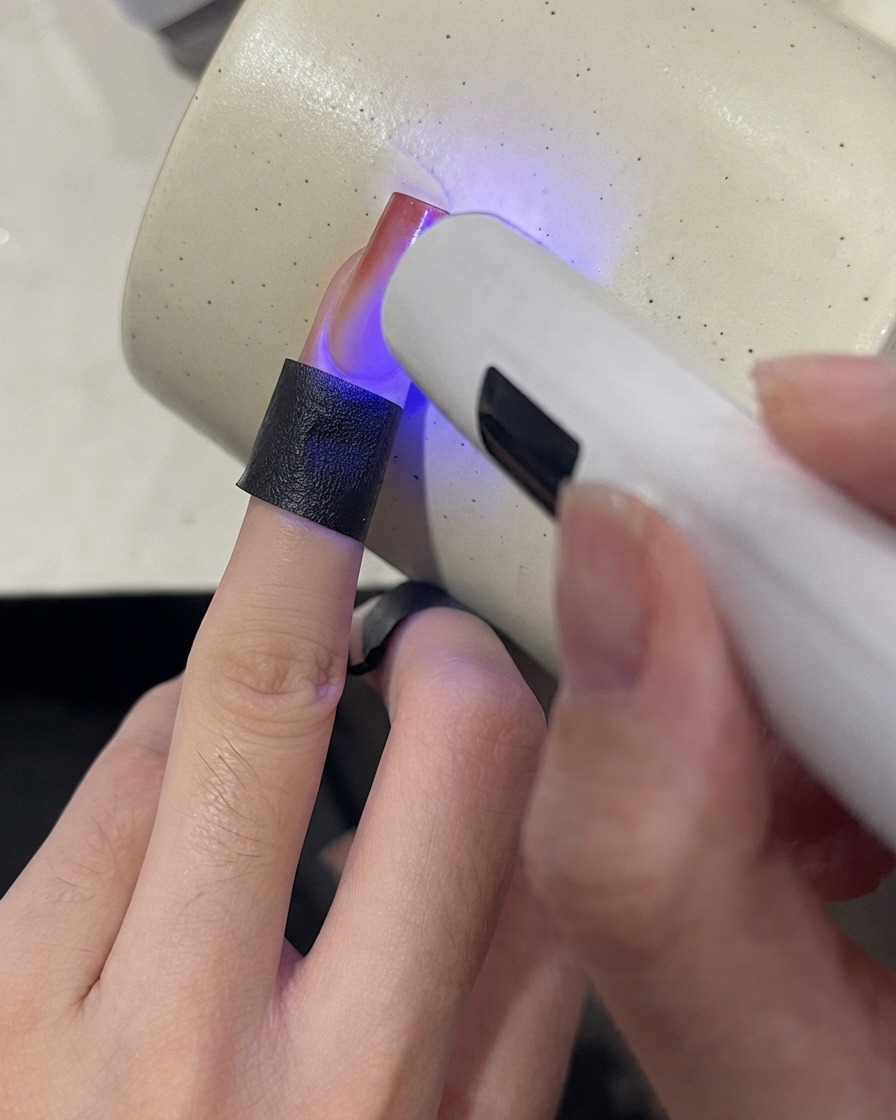Przenośna lampa UV utwardzająca końcówkę paznokcia z gradientem w kolorze winnej czerwoni.