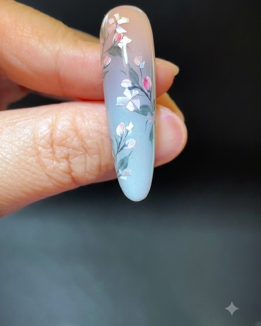 Dłoń z gotowym manicure z motywem muszli umieszczona w białej lampie utwardzającej UV/LED.