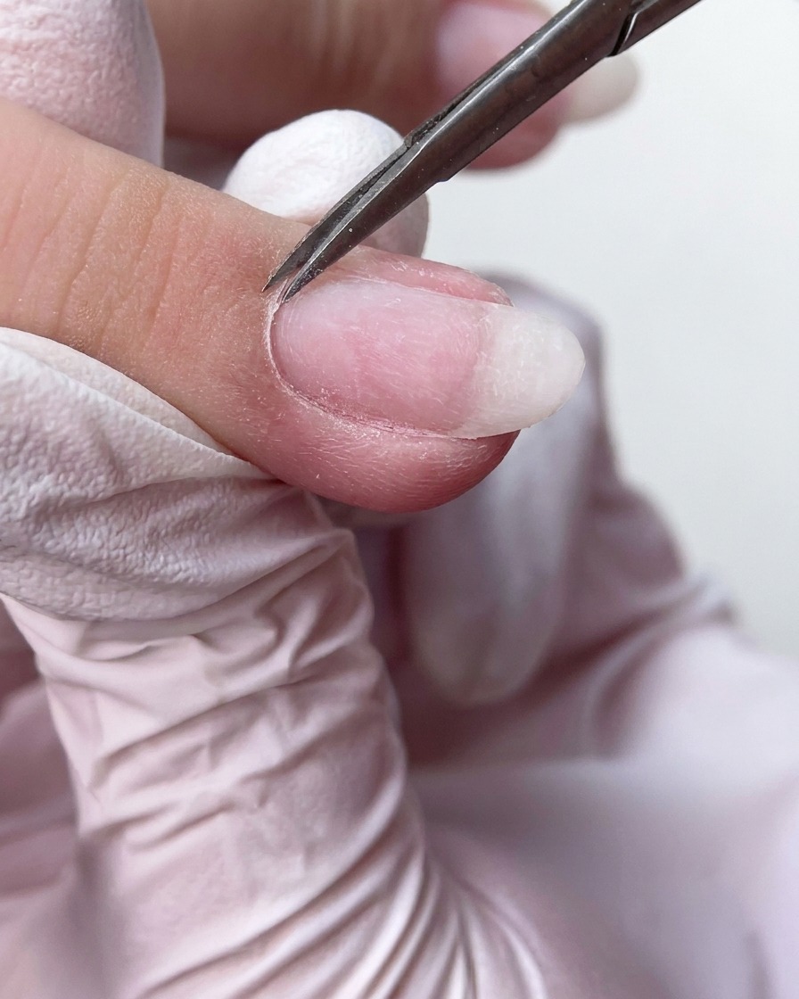 Precyzyjne cążki lub nożyczki do manicure starannie przycinające nadmiar martwego naskórka u nasady paznokcia.