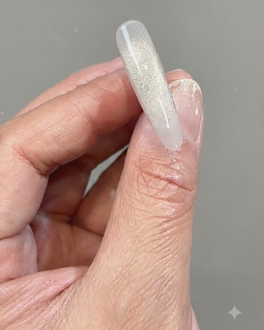 Dłoń trzymająca przezroczysty tip paznokcia z lśniącym, pionowym gradientem wykonanym z odblaskowego żelu shattered diamond.