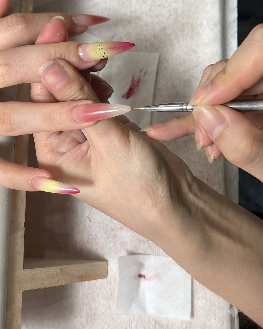 Cienki pędzelek do zdobień nakładający brązowe kropki jako pręciki na gradientowy paznokieć.