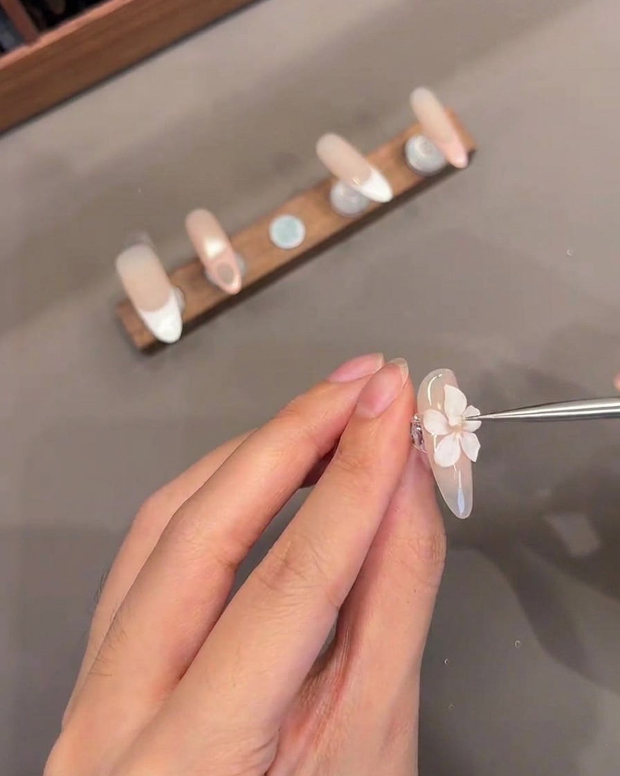 Zbliżenie cienkiego narzędzia dodającego mały biały żelowy środek do rzeźbionego kwiatka 3D na paznokciu.