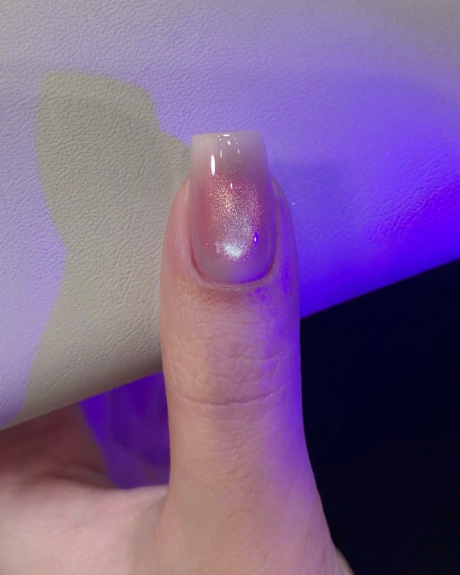 Kciuk pod fioletowym światłem lampy UV/LED, utwardzający świeżo zrobiony wzór kociego oka.
