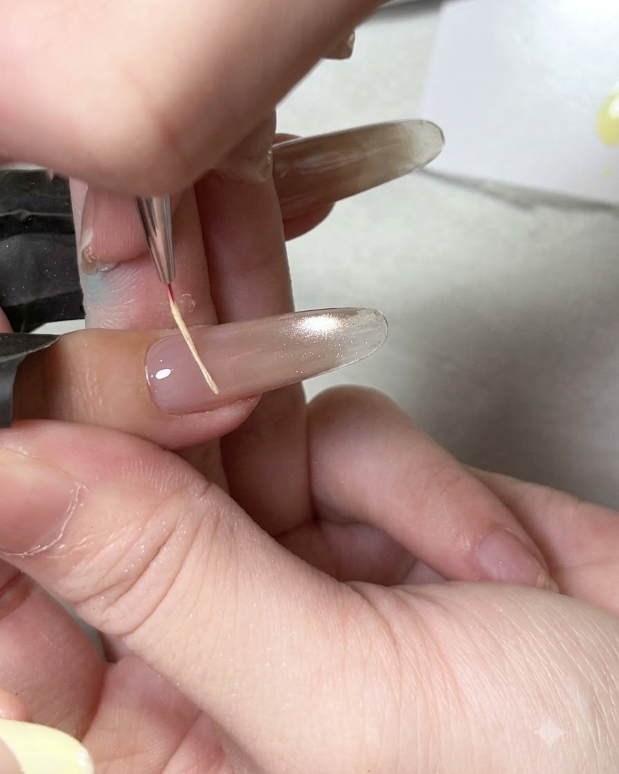 Cienki pędzelek do zdobień nakładający błyszczący top coat na utwardzoną bazę paznokcia cat eye.
