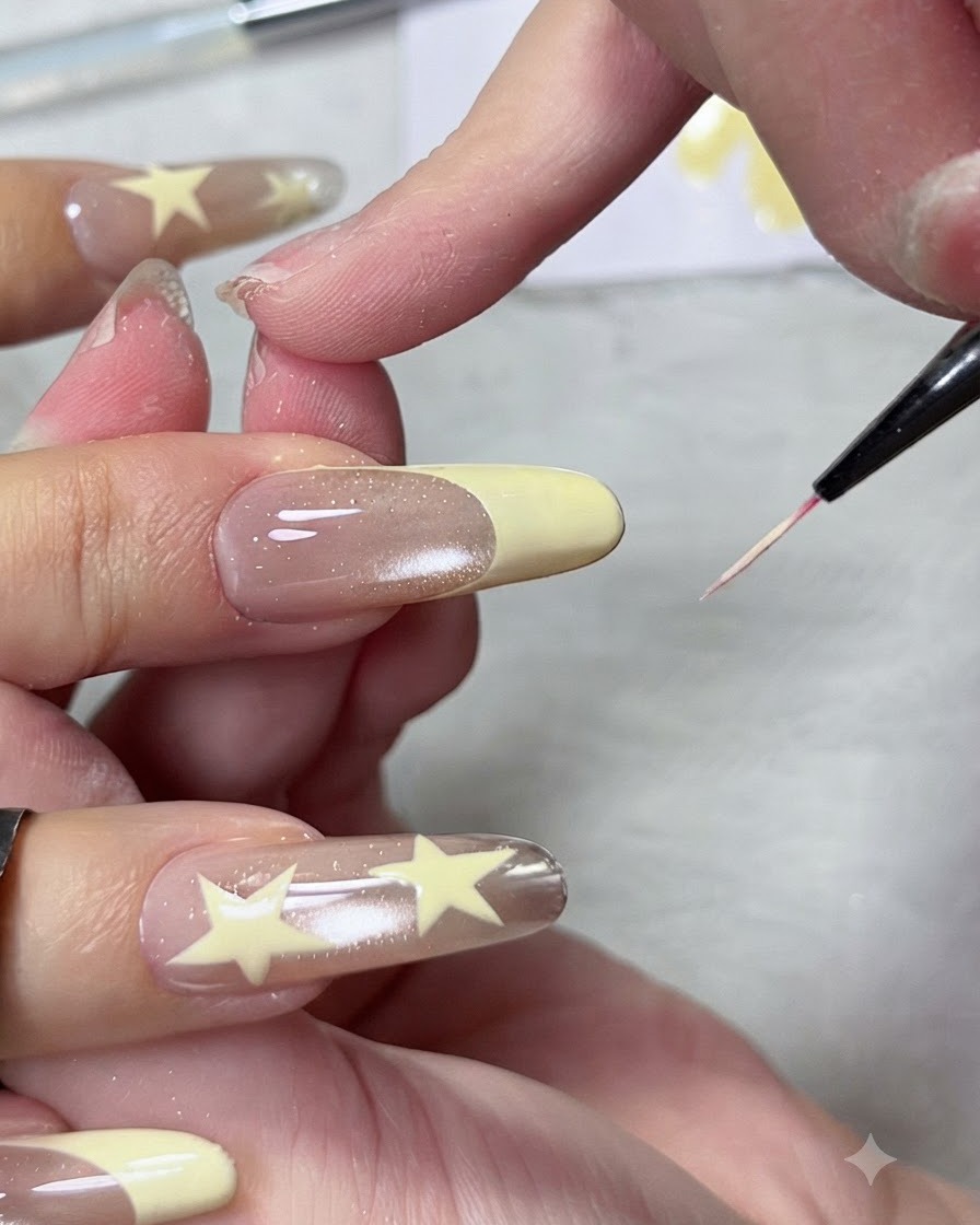 Zbliżenie cienkiego pędzelka liniowego modelującego i wyostrzającego linię uśmiechu pastelowo-żółtej końcówki manicure french na długim paznokciu migdałowym.