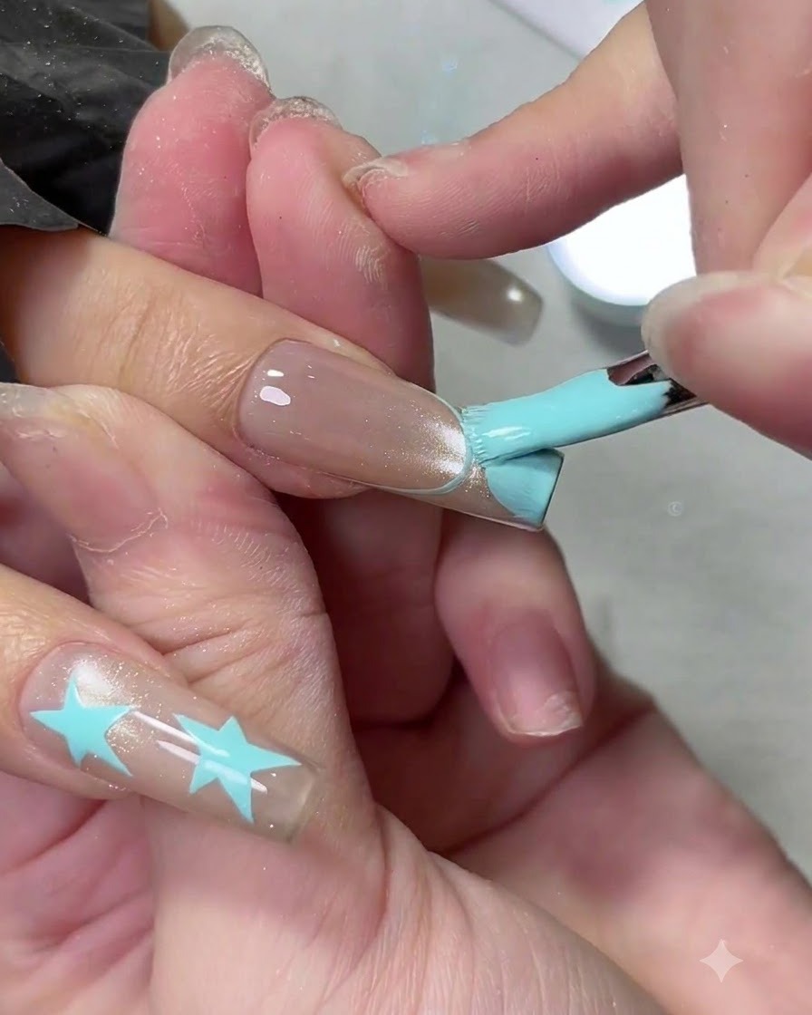 Płaski pędzelek żelowy wypełniający jasnoniebieską końcówkę manicure french na długim paznokciu.