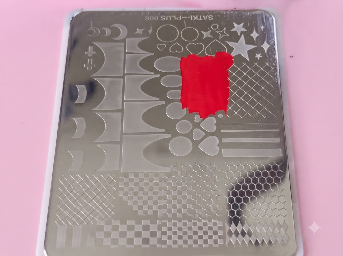 Przezroczysta plastikowa karta do skrobania przesuwająca się po metalowej płytce wypełnionej czerwonym lakierem.